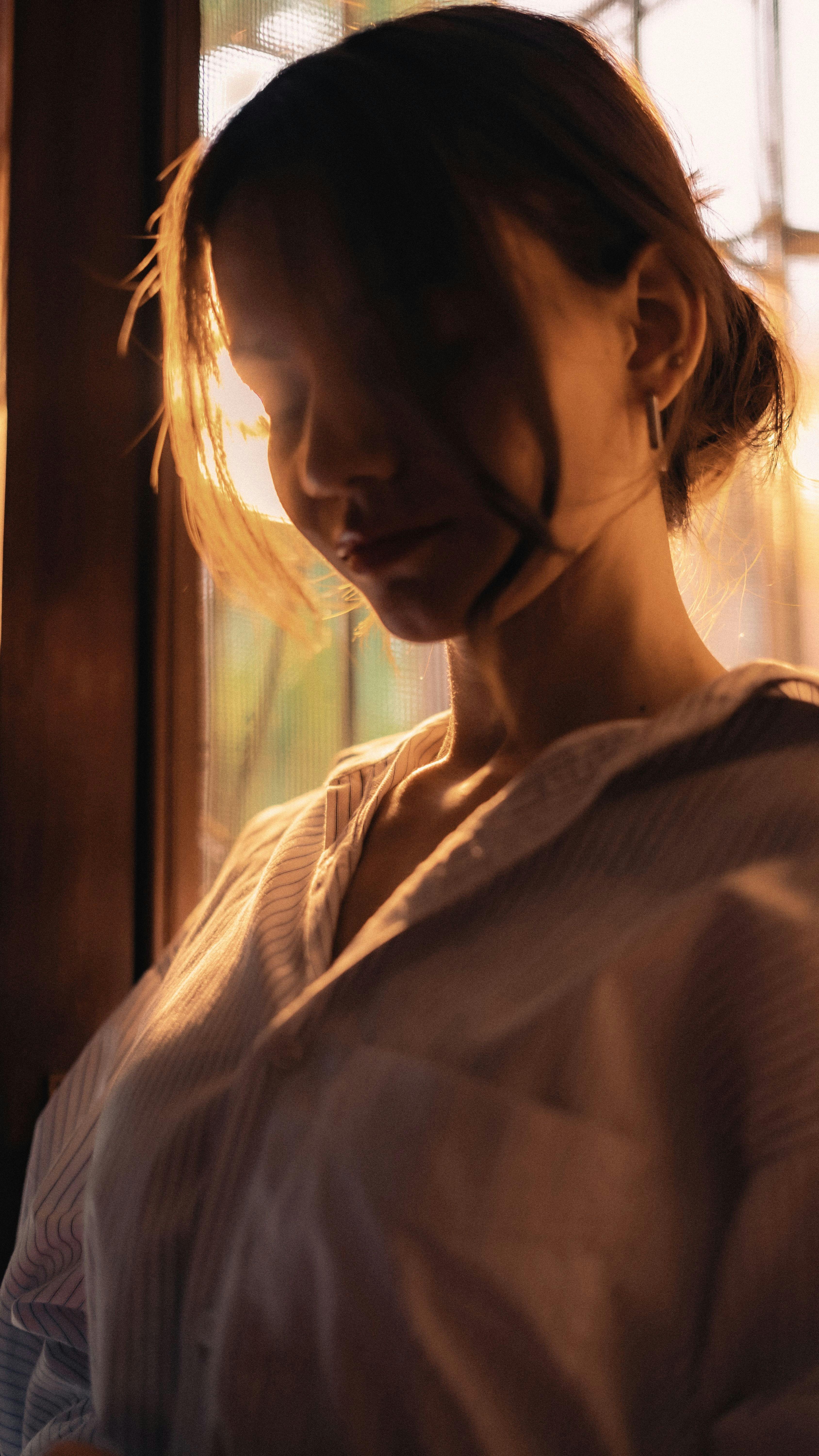 Woman in an open button-down shirt looking down in golden window light